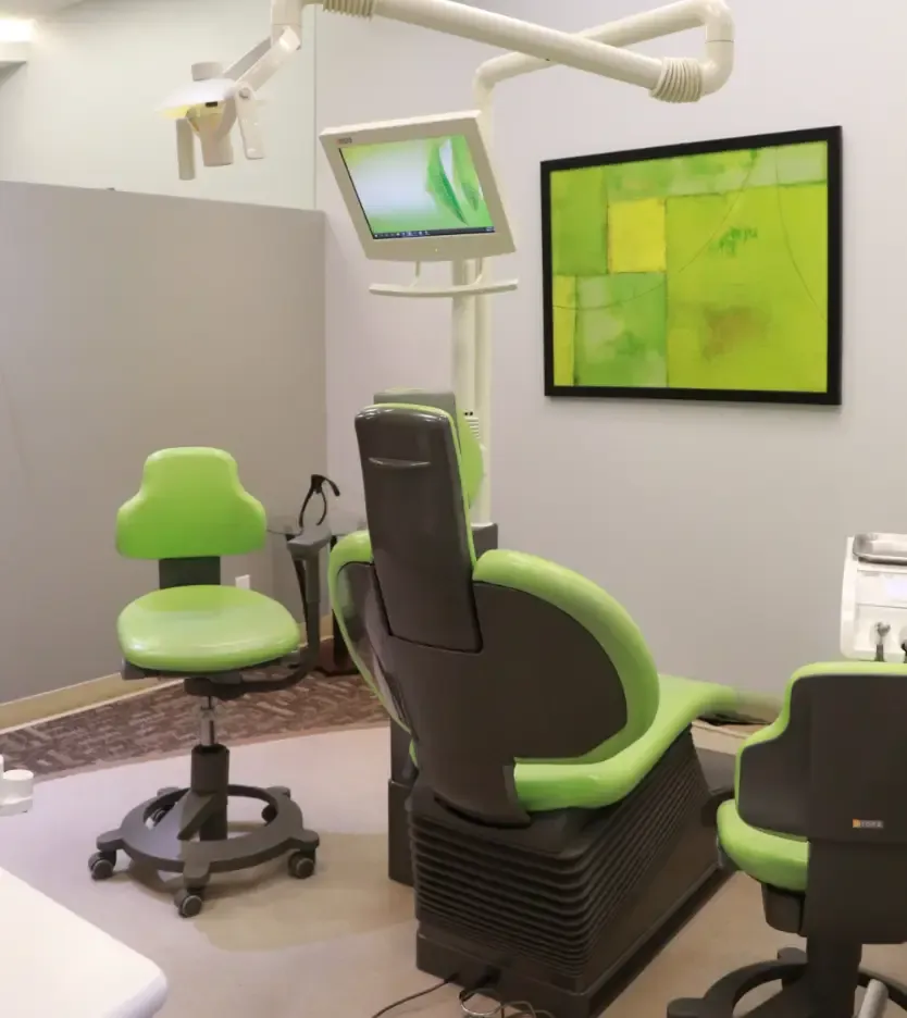Treatment room with a green patient chair and wall screen